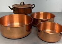 Small copper lidded pot with brass handles and three nesting copper mixing bowls shown together on surface.