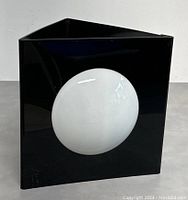 Front view of lamp showing black triangular frame with circular white globe inset