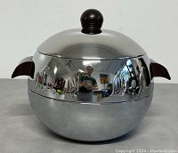 Front view of the chrome server showing spherical shape, wooden handles, and penguin engravings.