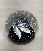 Clear glass paperweight with black and white internal swirls and air bubbles, angled view.