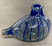 Close-up side view of blue and clear glass bird figurine showing vertical blue stripes and shape of the figurine.