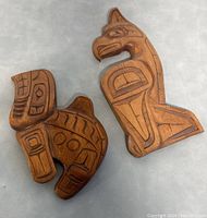 Two hand carved wooden Northwest Coast figures showing front details and patterns of the carved Thunderbird and another figure.