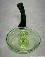 Photo of the uranium Vaseline depression glass dish with heart-shaped handle showing the green translucent glass and scalloped edge.