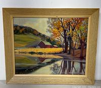 Full view of framed painting showing rural landscape with barn, trees, and water reflection.