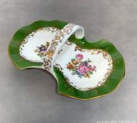 Porcelain dish with green edges, gold detailing, and floral handpainted design, showing the handle and scalloped edges from a side angle