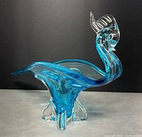 Front angle view of the aqua blue Murano glass bird centerpiece, showing curved body and clear glass feet and crest.