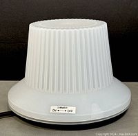 Front view of the white ribbed cylindrical tone knob lamp with dimmer switch label shown on the base.
