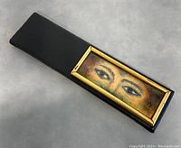 Overall angled view of the plaque showing the black textured base and inset painted eyes panel with gold frame.