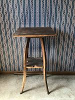 Full view of antique wooden stand showing square top, curved legs, and scalloped lower shelf against patterned wallpaper.