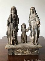 Front view of three carved wood Santos figures (Joseph, child Jesus, Mary) mounted on rectangular wood base.