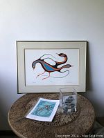 Full view of framed print, glass vase, and art card on a carved wood table