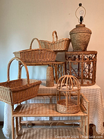 Photo showing assorted wicker and rattan decor including baskets, stool, bird cage, woven lamp base, and decorative wind chime arranged on and around a table.