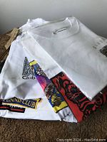 Stack of various white souvenir t-shirts featuring different colorful prints, some still packaged.