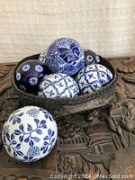 Seven ceramic carpet balls arranged in a dark woven basket on a carved wooden surface, showing various blue and white patterns.