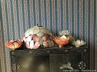 Full view of the round capiz shell lampshade and the four small capiz votive holders arranged on a black painted floral cabinet.