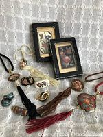 Photo showing an assortment of vintage cloisonné enamel jewelry items including tassel necklaces, earrings, framed floral artworks, and a small vial, all placed on a white textured background.