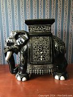 Side view of the black elephant ceramic stool showcasing the gold and white painted details and ornate carvings.