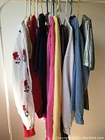 Full side view of vintage women's tops hung on hangers showing different colors and styles including embroidered blouse and various knits and shirts.
