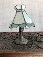 Front side view of vintage lamp showing metal base and stained glass shade with scalloped green edge and hanging glass drops.