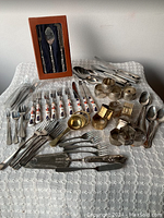 Full lot of vintage tableware and serving pieces arranged on cloth with napkin rings, cutlery, and boxed serving utensils