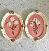Both vintage chalkware plaques showing the white and gold oval frames, pink textured backgrounds, and 3D white floral designs