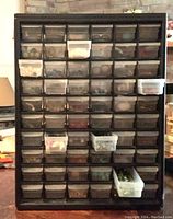 Front view of black tool case with 60+ translucent small drawers filled with beads, some drawers taped shut.