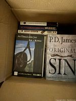 Photo of the collection of P.D. James hardcover books in a box, showing titles An Unsuitable Job for a Woman and Original Sin.