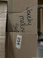 Photo of a cardboard box with handwritten label 'Jewelry making sup'.