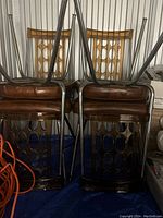 Photo showing backs of six chairs stacked upside down, featuring Lucite backs with oval cutouts and chrome legs with brown cushioned seats.