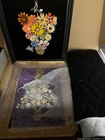 Photo showing two black framed jewelry trees, one with colorful fabric flowers arranged as a bouquet and the other partially covered with bubble wrap showing sparkly jewelry tree on purple quilt fabric.
