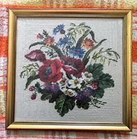 Full square needlepoint floral artwork in gold-tone wood frame under glass, showing the entire piece with various flowers in shades of red, blue, white and green foliage.