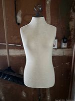 Front view of fabric-covered female torso mannequin with decorative finial and adjustable metal stand, showing some surface wear.