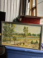 Full view of the framed painting depicting landscape with trees and water body.