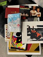 Overview showing stacked colorful art prints, an original painting, a dog screen print, a Vogue print and two vintage art supply sets (Pentel pastel dye sticks and a Mrie Bros pigment bottle set)