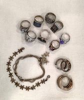 Photo showing 8 rings with various designs, 2 star-themed bracelets, and 2 pairs of hoop earrings on fabric background.