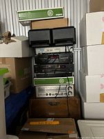 Stack of stereo equipment including black speakers on top, several black audio components, and a wooden receiver at bottom with boxes surrounding.