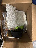 Box containing beige lace fabric accessory on top along with black and gold fabric accessories