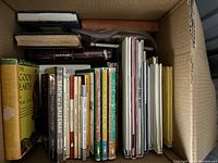 Top view of a cardboard box showing a variety of vintage and collectible books arranged vertically, with children’s books and classic titles visible