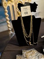Photo of layered gold-tone chain necklaces on black display stand including snake pendant, gemstone charms, heart pendant, and multiple chains