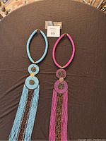 Photo of two South African beaded handmade necklaces laid flat on a dark surface, one blue and one pink with long fringes and circular beadwork