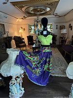 Mannequin dressed in African print cotton skirt and lime green top, displayed in room with vintage furniture and stained glass window.