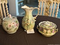 Front view of three porcelain pieces on black cloth showing floral decorations and gold trim.