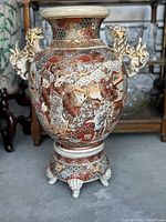 Front angle of the larger antique Satsuma pot showing Foo Dog handles and colorful hand-painted scenery.