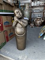 Full view of the pewter Asian figurine standing on the floor near boxes and other decorative items