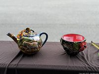 Ceramic teapot and flower bowl displayed on table showing detailed 3D animal and floral decorations, colorful finish and handmade craftsmanship.