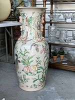 Front view of Chinese enameled porcelain vase showing colorful bird, butterfly and fruit designs with pink foo dog handles on neck.