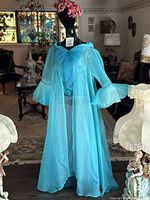 Front view of mannequin wearing turquoise sheer long robe with bell sleeves, displayed indoors