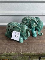 Side and front view of sitting and standing teal ceramic elephant figurines with intricate cut-out patterns on their backs.