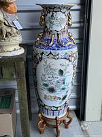 Full view of ornate oriental vase with floral and bird paintings, gold handles, and wooden base.