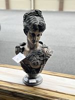 Front view of bronze bust sculpture showing intricate facial features and floral patterns on dress and hair.
